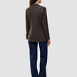 Back view of a woman wearing a Women Serene Blazer Regular Walnut Herringbone, dark blue jeans, and brown shoes.