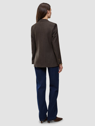 Back view of a woman wearing a Women Serene Blazer Regular Walnut Herringbone, dark blue jeans, and brown shoes.