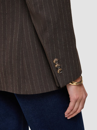Close-up of a brown Women Serene Blazer Regular Walnut Herringbone featuring three buttons on the sleeve cuff, worn with dark denim jeans.