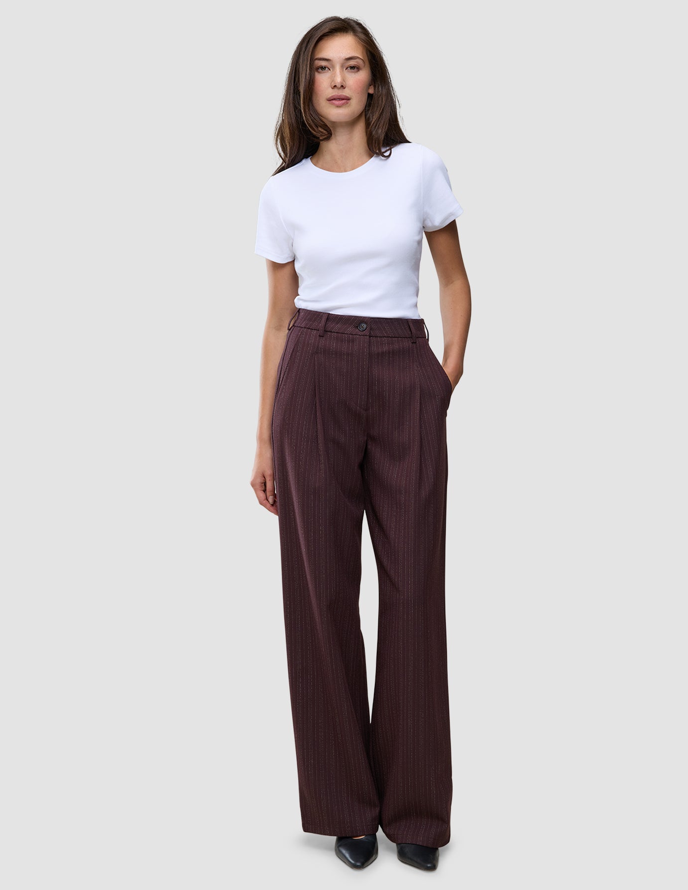 A woman wears a white t-shirt and Women Serene Pants Wide Berry Pinstripe, featuring a wide-leg, high-waisted design that reflects a clean Scandinavian aesthetic.