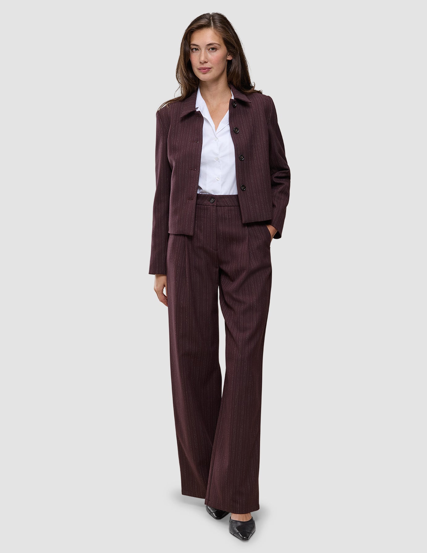 A woman wears a dark pinstriped Women Serene Pants Wide Berry Pinstripe blazer and matching wool-like wide-leg trousers over a white collared shirt.