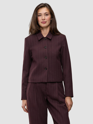 A woman wears the Women Serene Short Jacket Berry Pinstripe, a berry-colored, button-front short jacket in a Scandinavian design with thin vertical pinstripes.