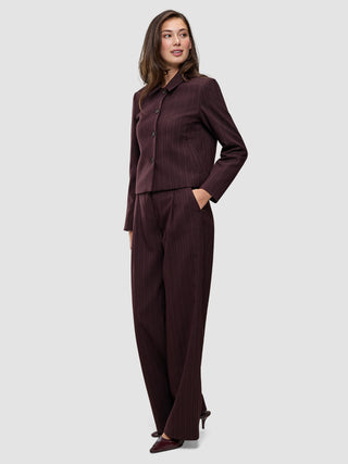 A woman wears a Women Serene Short Jacket Berry Pinstripe in a dark berry-colored Scandinavian design, paired with matching wide-leg trousers.