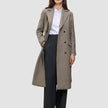 A person wearing a Women Wool Coat Greige in a long, double-breasted style over a white collared shirt and black trousers.
