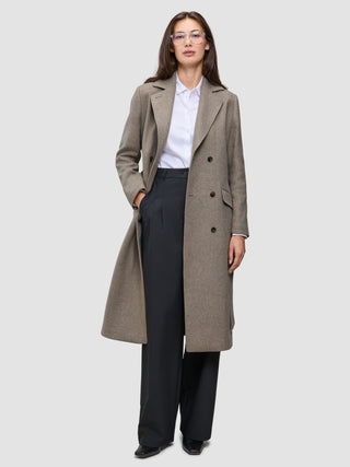 A person wearing a Women Wool Coat Greige in a long, double-breasted style over a white collared shirt and black trousers.