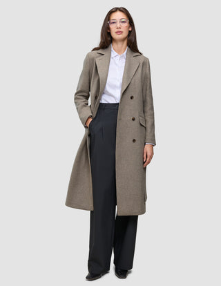 A person wearing a Women Wool Coat Greige in a long, double-breasted style over a white collared shirt and black trousers.