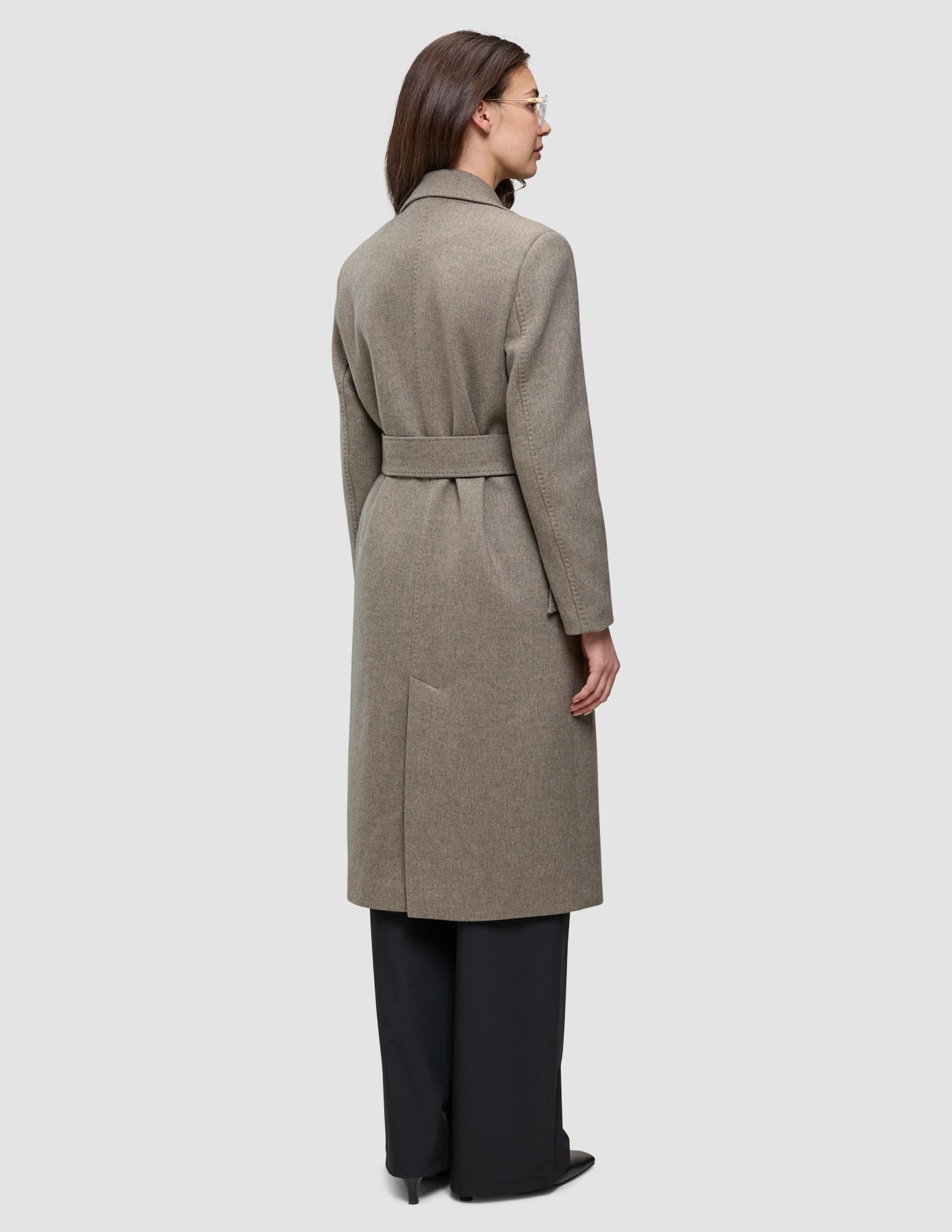 A person viewed from the back wearing a Women Wool Coat Greige, a long, double-breasted wool coat with a belted waist over dark trousers.