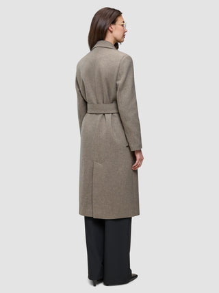 A person viewed from the back wearing a Women Wool Coat Greige, a long, double-breasted wool coat with a belted waist over dark trousers.