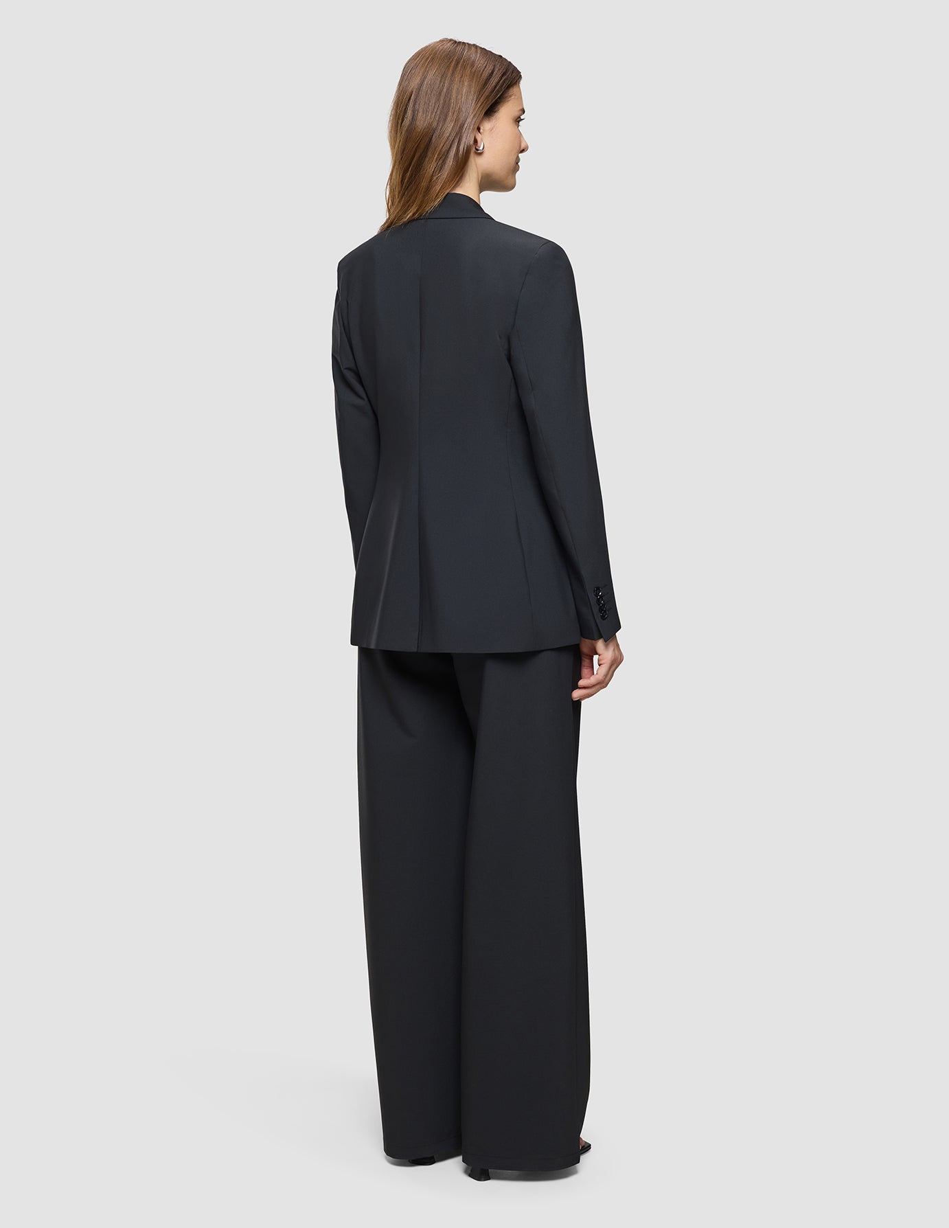 A woman seen from behind wearing a Women’s Avira Blazer Black and matching wide-leg trousers.