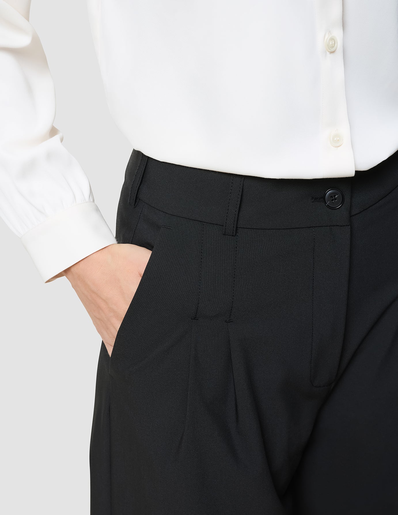 A white long-sleeved button-down shirt tucked into Women’s Avira Pants Wide Black with a hand resting in the pocket.