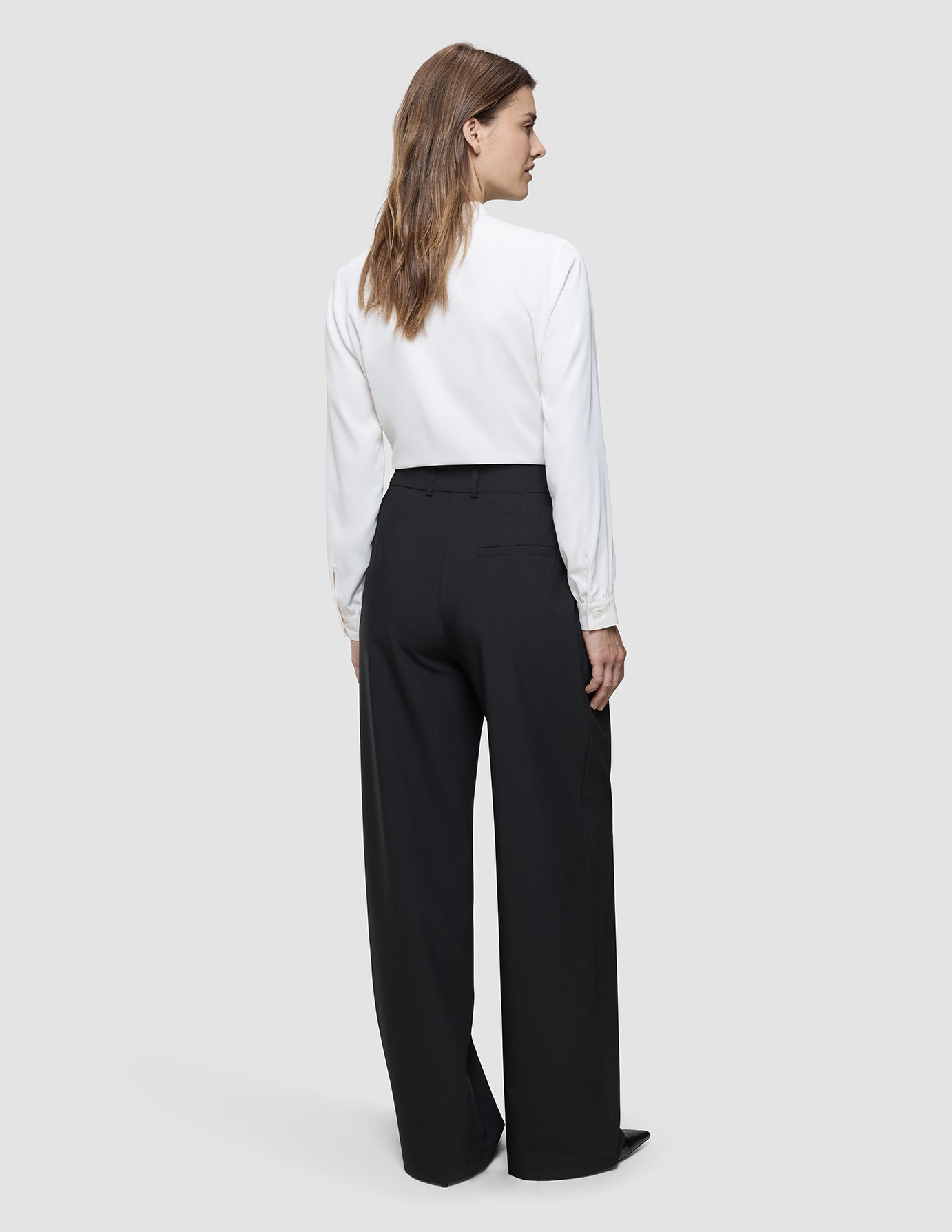 A woman seen from behind wearing a white long-sleeved button-up shirt tucked into black Women’s Avira Pants Wide Black.