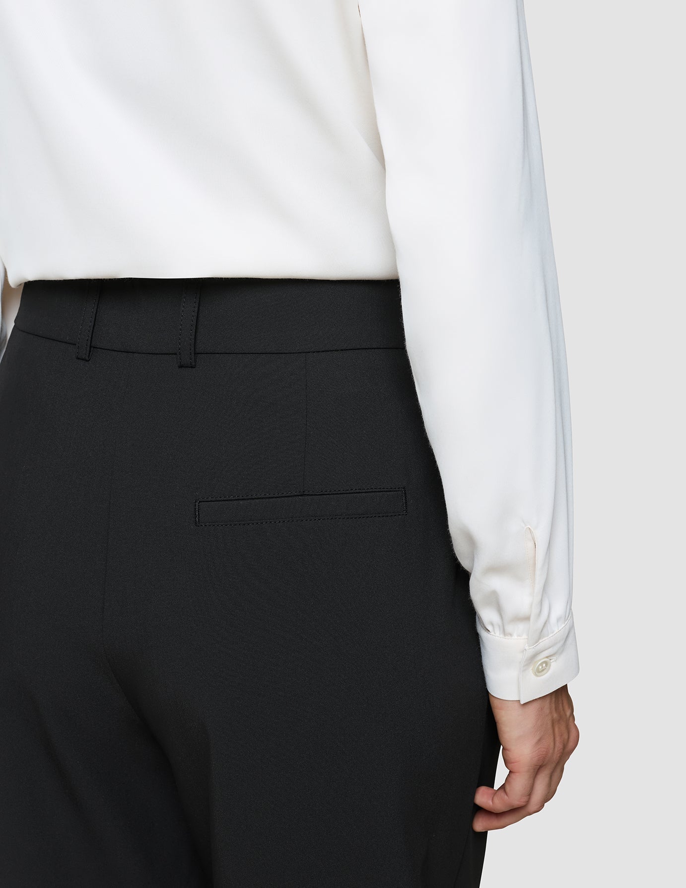 A person wearing a white long-sleeved shirt tucked into Women’s Avira Pants Wide Black with a back pocket.