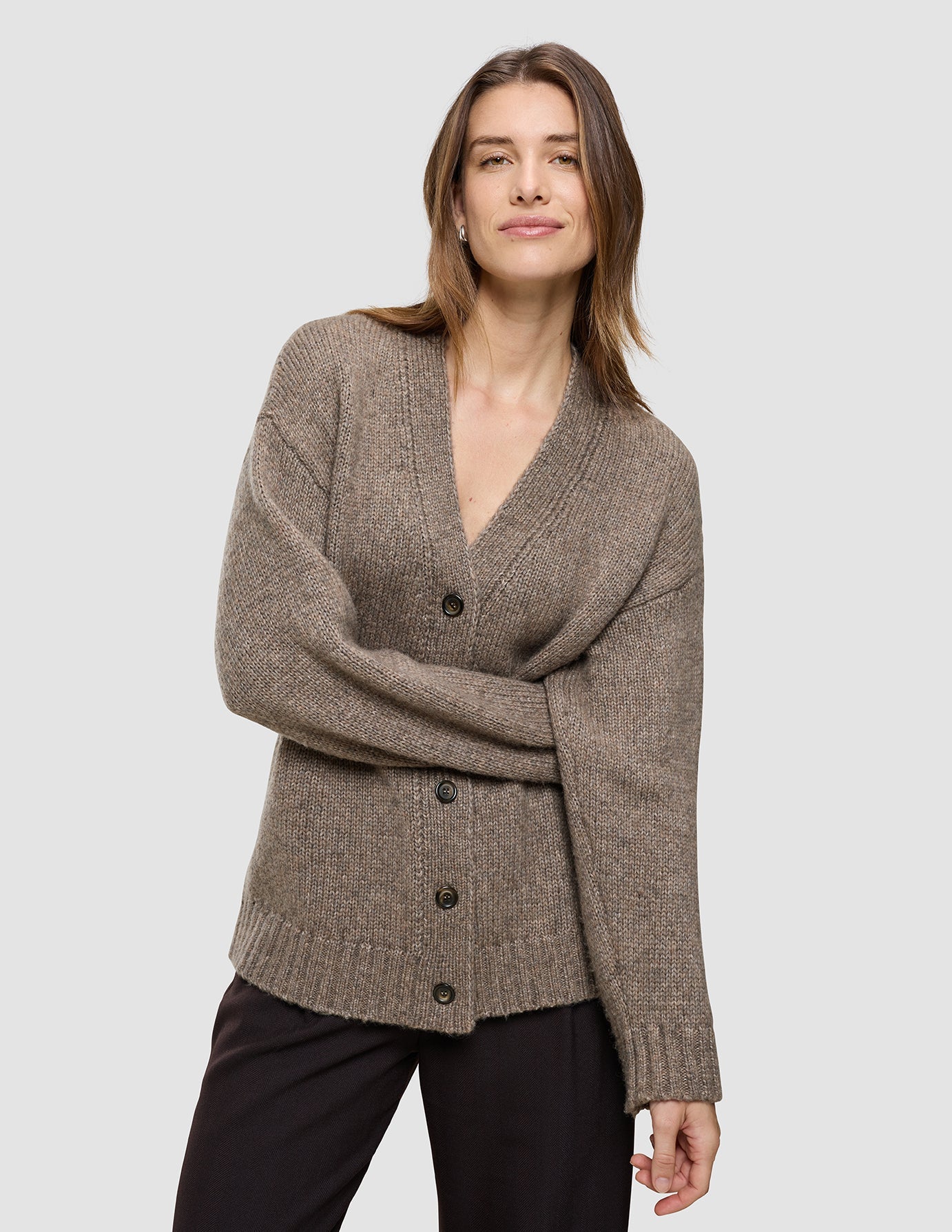 A person wearing a Women’s Chunky Soft Wool Knit Cardigan Taupe Melange, featuring a cozy, taupe V-neck merino wool design with a button-front closure.