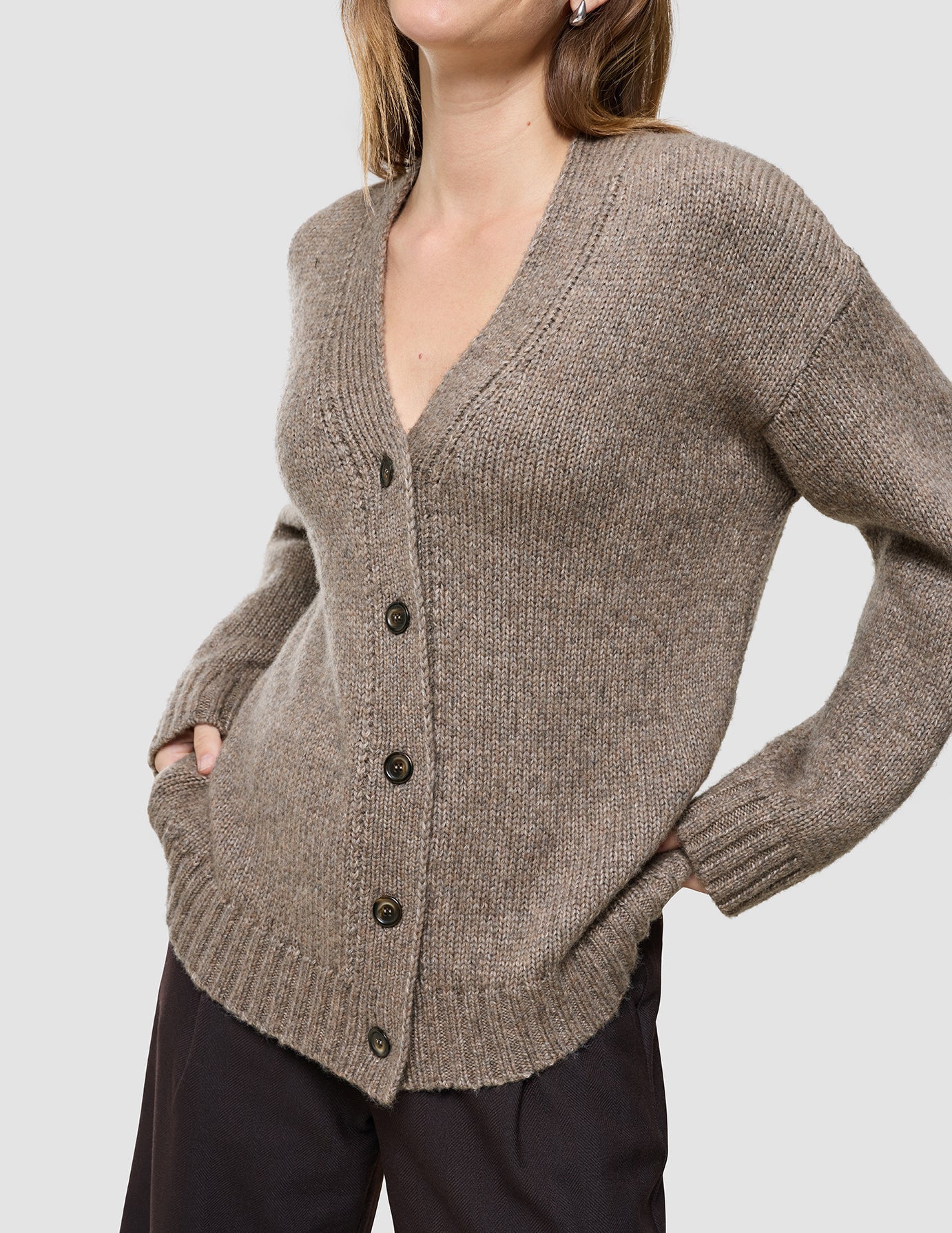 A person wearing a Women’s Chunky Soft Wool Knit Cardigan Taupe Melange, featuring a cozy, v-neck chunky wool design with button closures and side pockets.