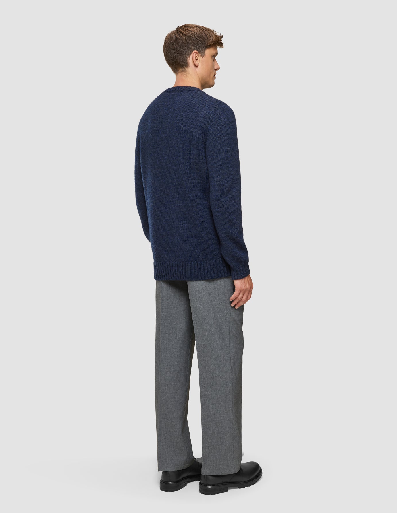 A man viewed from behind, wearing a Chunky Soft Wool Knit Crewneck Dark Navy Melange, gray trousers, and black shoes.