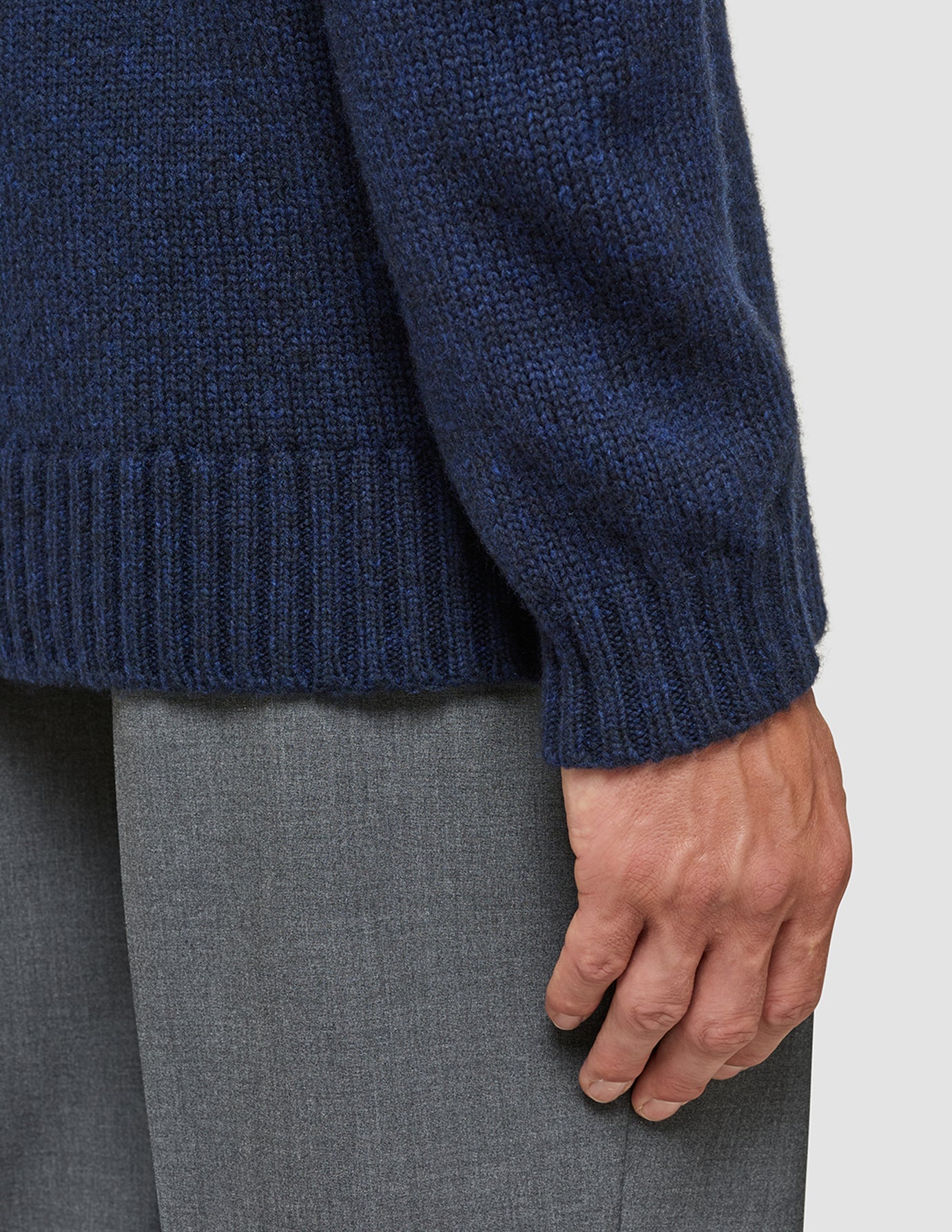 A person wearing a Chunky Soft Wool Knit Crewneck Dark Navy Melange with a chunky, textured knit finish and ribbed cuffs over grey trousers.
