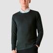 Model seen from the front wearing a dark green crewneck in fine knit with a white shirt underneath