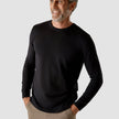 Model seen from the front wearing a black crewneck in fine knit with a white shirt underneath