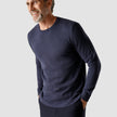 Model seen from the front wearing a navy blue crewneck in fine knit with a white shirt underneath