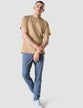 Model in full body wearing sand grain t-shirt with blue pants and white sneakers, the t-shirt has the company logo across the chest