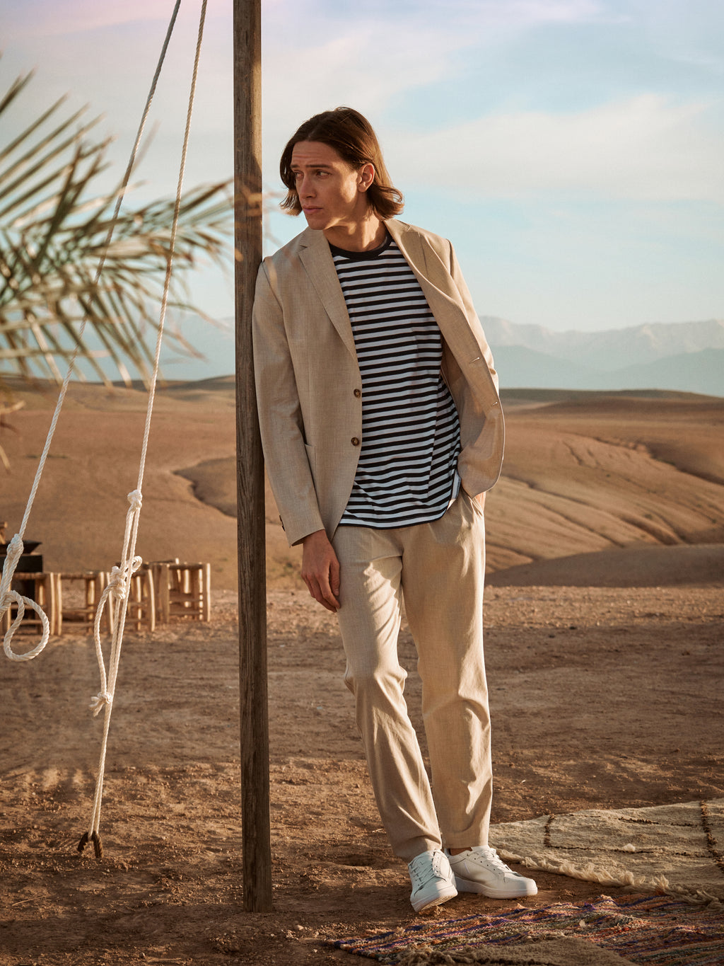 Male wearing beige pants, beige blazer and striped T-shirt in a desert