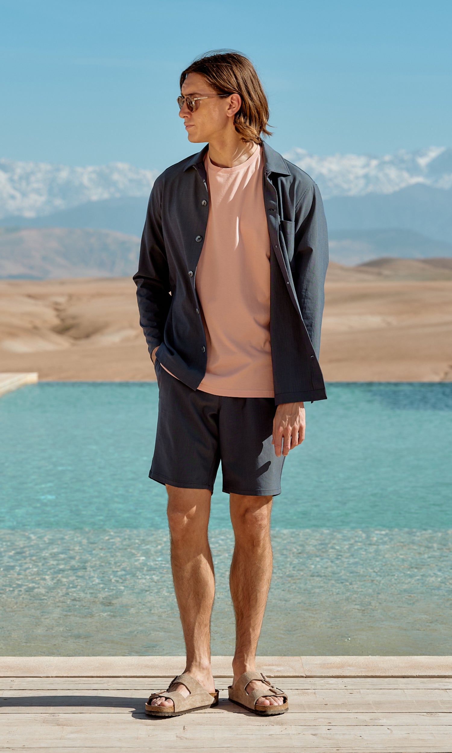 Male model wearing navy shorts, navy overshirt and coral T-shirt standing in a summer nature setting