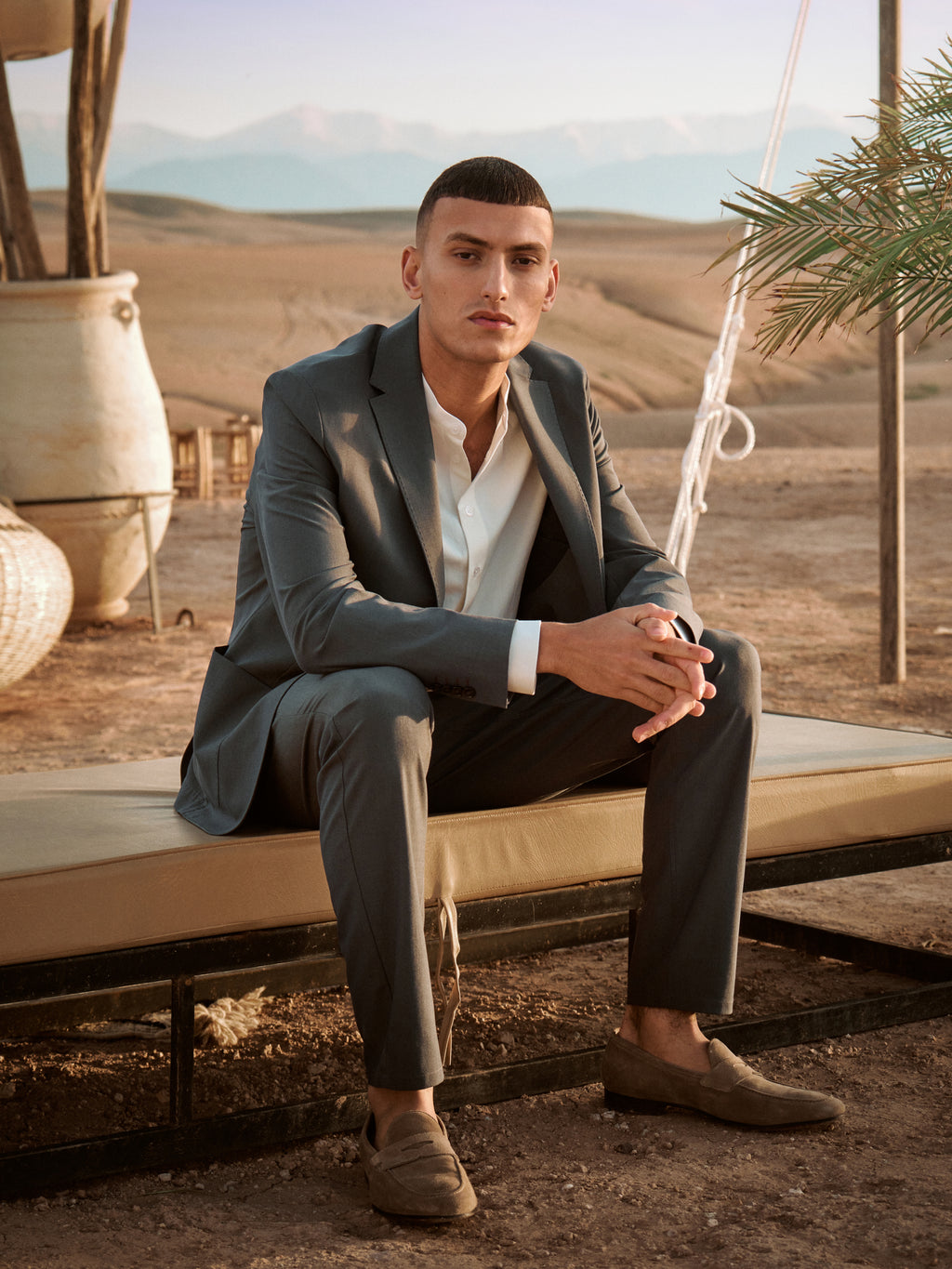 Male model wearing navy suit and white shirt sitting on a chair in the desert