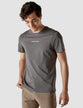 Model wearing dark grey t-shirt seen from the front the t-shirt has the company logo across the chest