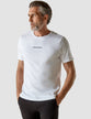 Model wearing white t-shirt seen from the front the t-shirt has the company logo across the chest