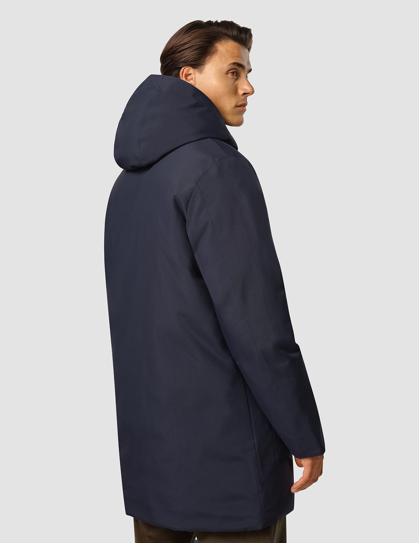 A person shown from the side, wearing a dark navy Utility Jacket Dark Navy hooded utility jacket with PrimaLoft insulation.