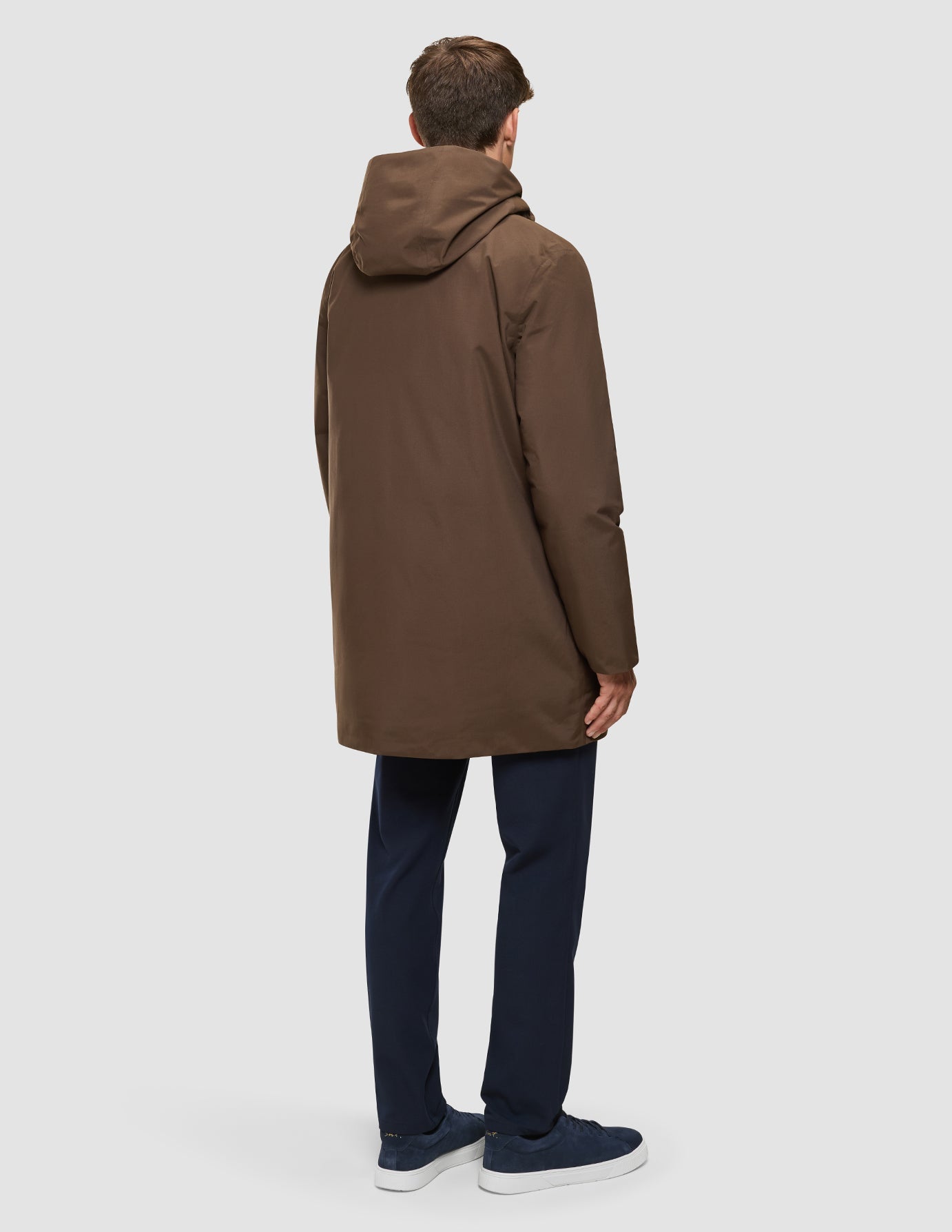 A person seen from behind wearing a brown, waterproof Utility Jacket Saddle Brown, dark trousers, and dark sneakers.