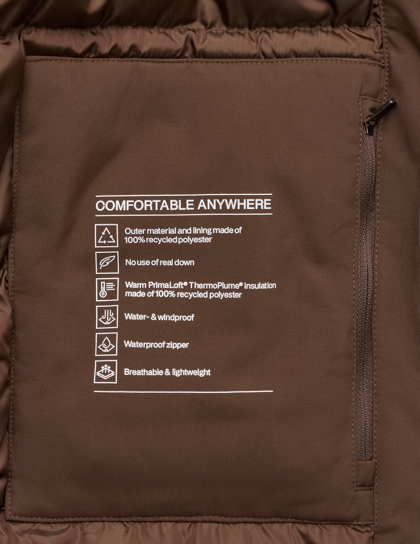 Interior pocket of a saddle brown Utility Jacket with a printed label titled COMFORTABLE ANYWHERE, detailing recycled polyester material, synthetic insulation, and water-resistant properties.