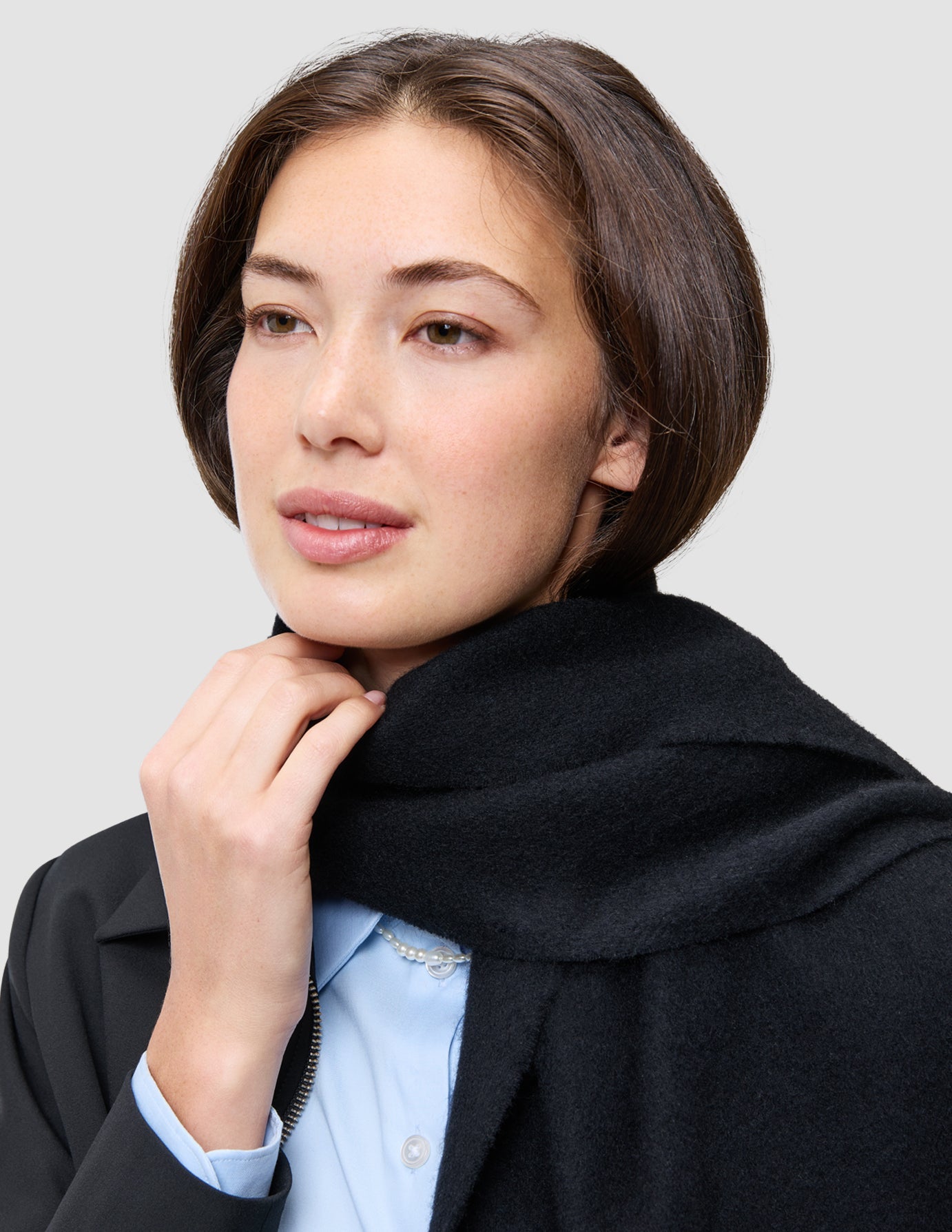 A person wearing a black scarf draped over an An easy office upgrade zip jacket and a light blue Oxford shirt.