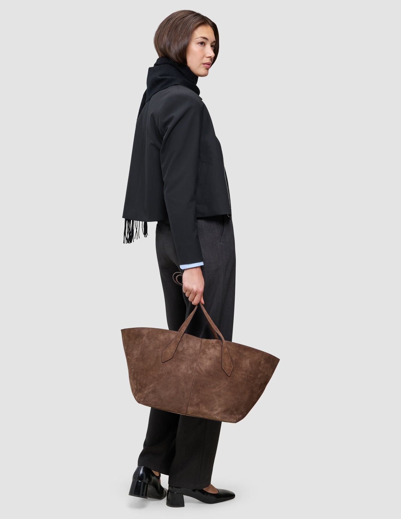 A person in an An easy office upgrade Essential Zip Jacket and dark trousers carries a large brown tote bag.