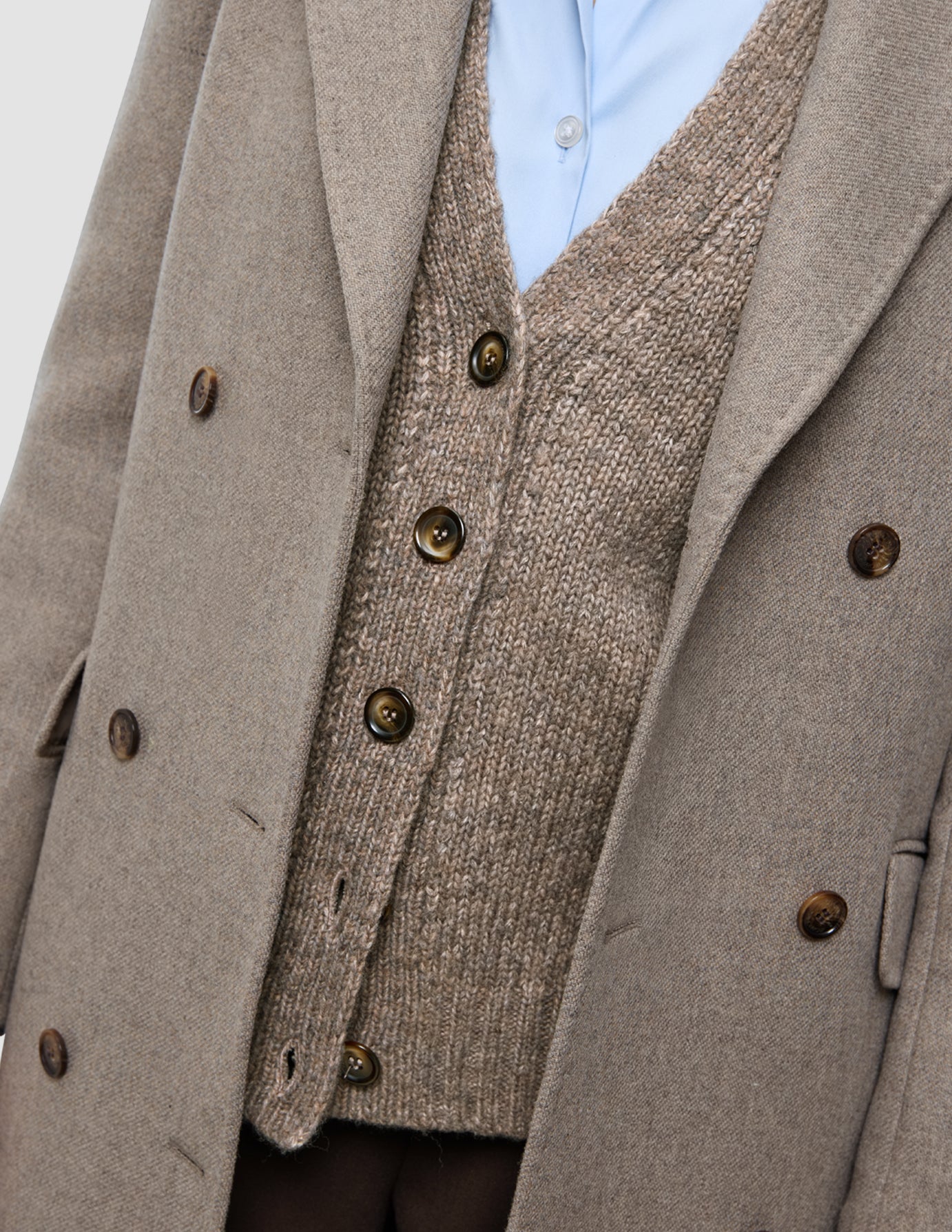 Cold-weather workwear consisting of a double-breasted wool coat worn over a button-up cardigan and light blue Oxford shirt.