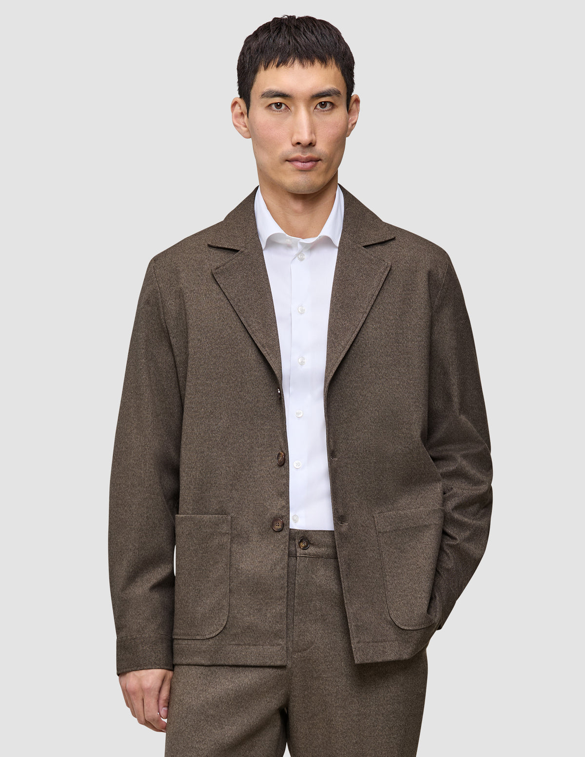 A man wearing a dark beige Atelier Overshirt heavyweight twill blazer over a white collared shirt.
