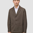 A man wears a brown Atelier Overshirt Dark Beige heavyweight twill blazer with large patch pockets over a white collared shirt.