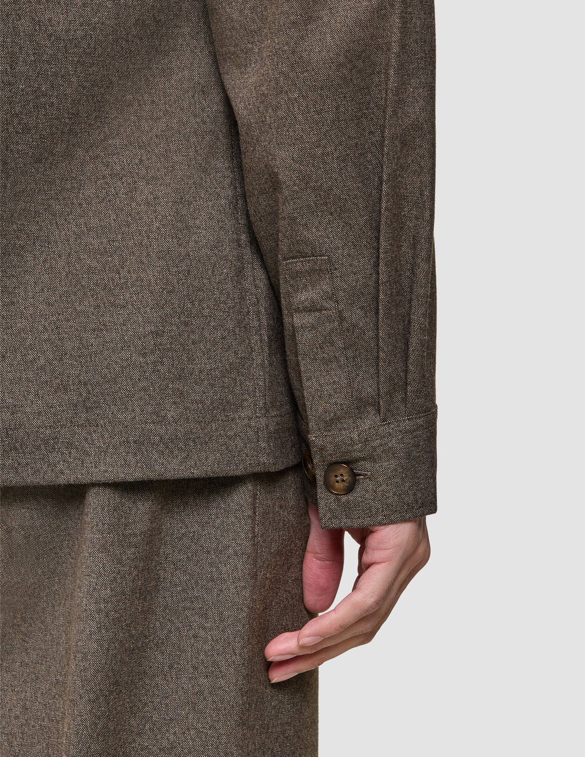 A close-up of a person wearing an Atelier Overshirt Dark Beige, a brown, heavyweight twill long-sleeved shirt with buttoned cuffs.