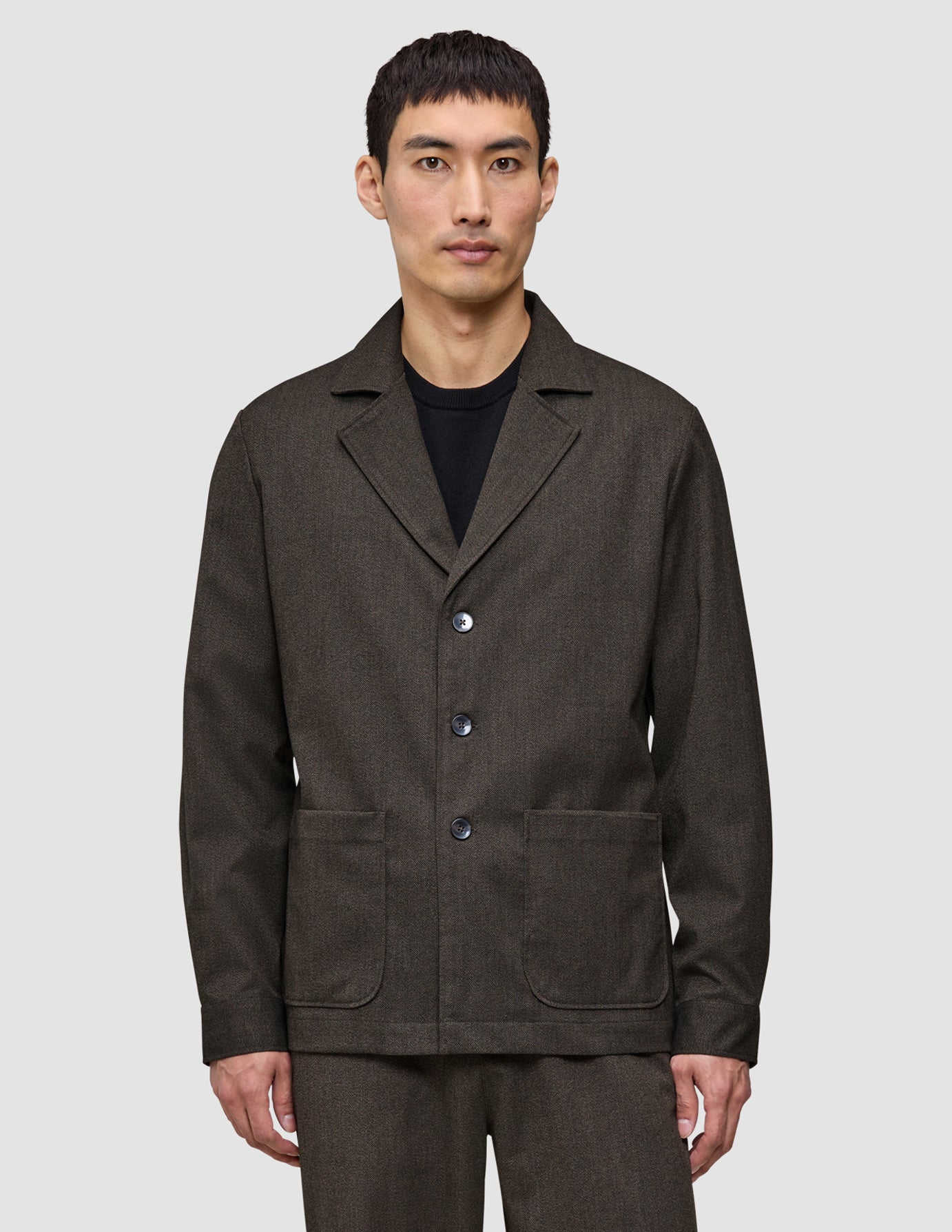 A man wears the Atelier Overshirt Dark Brown, a heavyweight textured blazer featuring three front buttons and two large patch pockets.