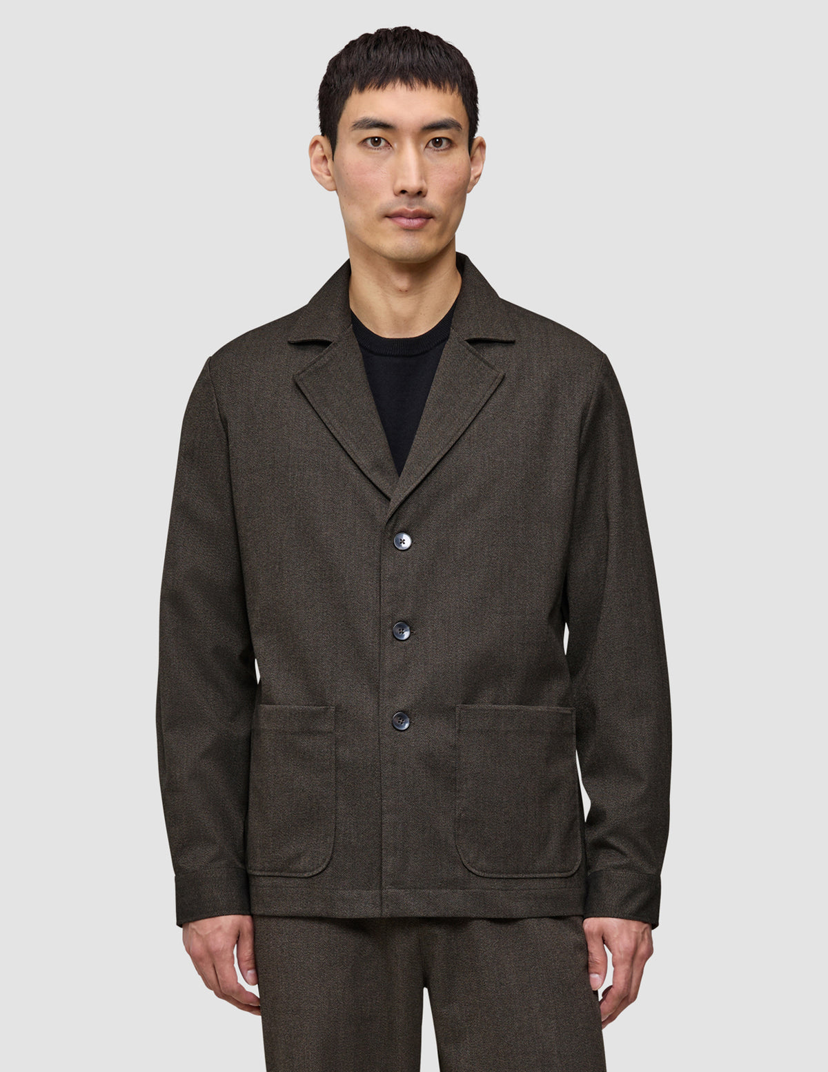 A man wears the Atelier Overshirt Dark Brown, a heavyweight textured blazer featuring three front buttons and two large patch pockets.