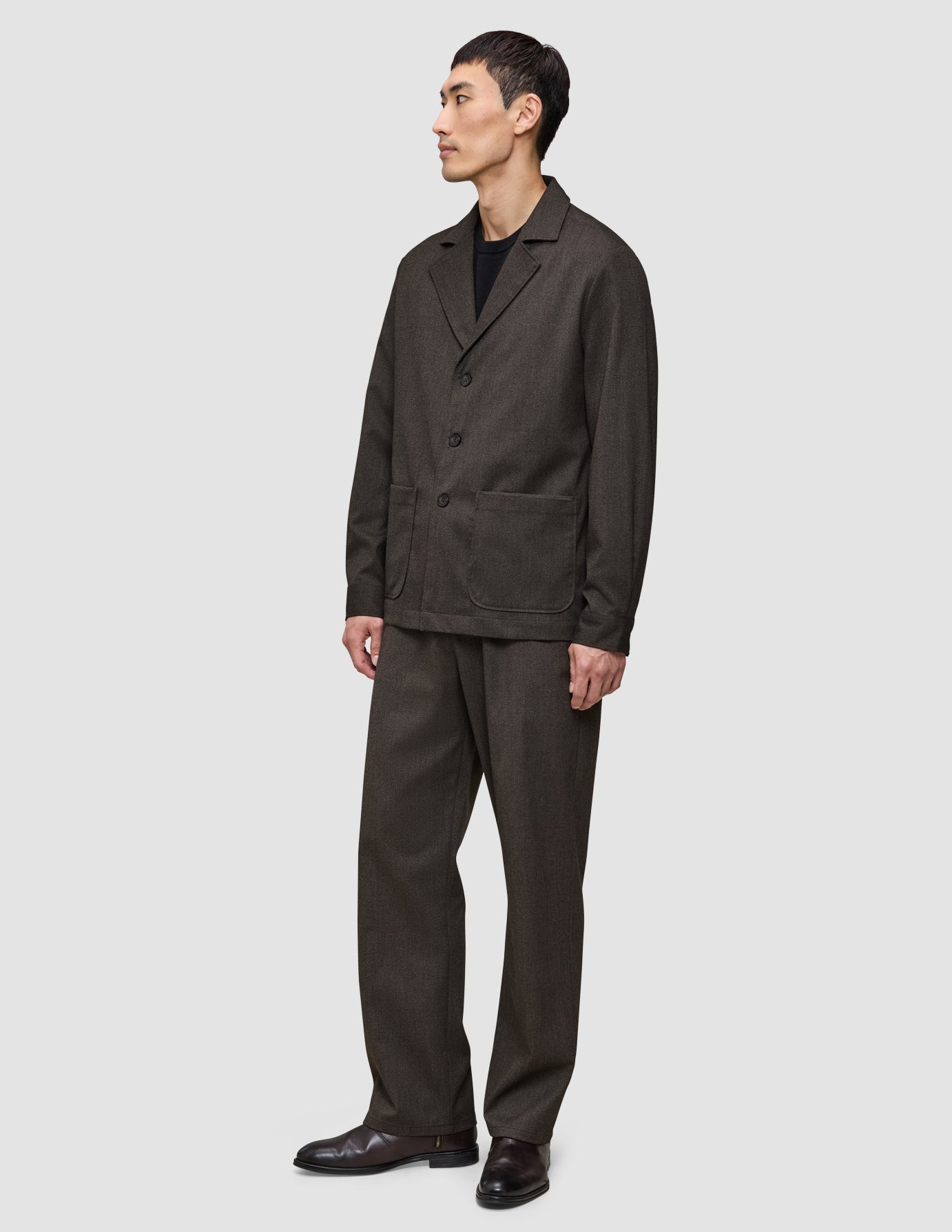 A person wearing a heavyweight, textured dark brown Atelier Overshirt and matching trousers over a black shirt.