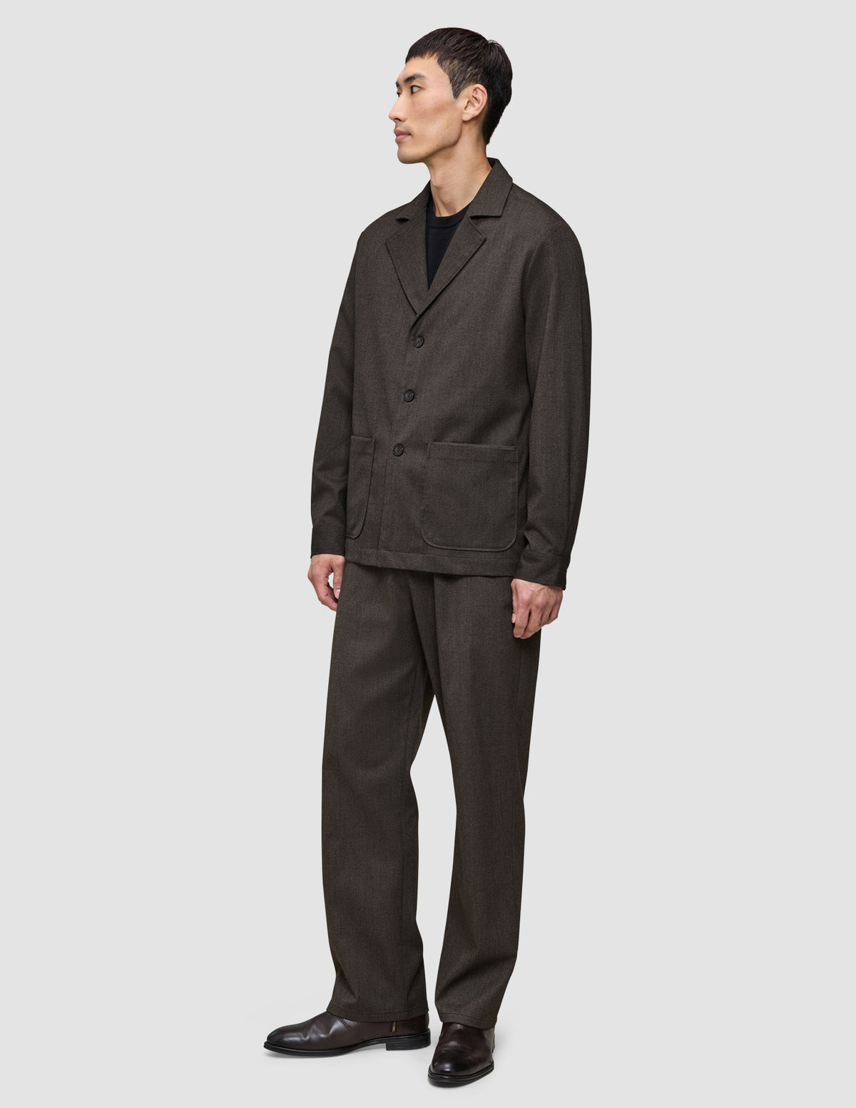 A person wearing a heavyweight, textured dark brown Atelier Overshirt and matching trousers over a black shirt.