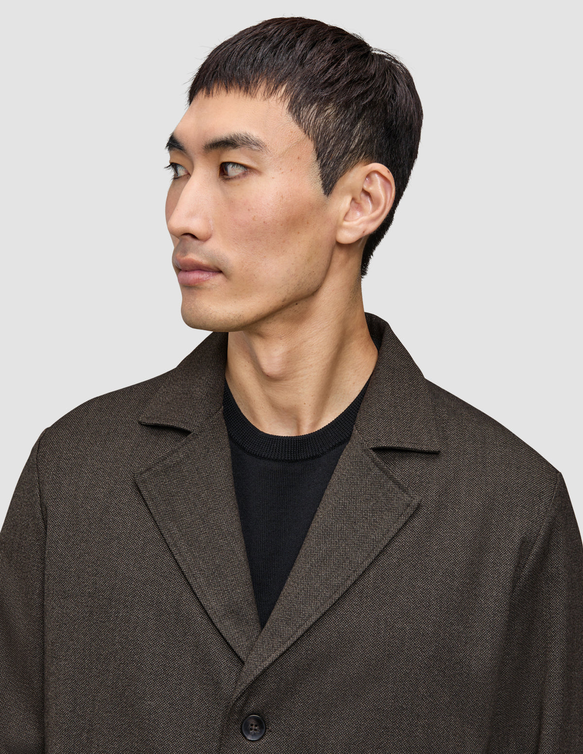A man wears an Atelier Overshirt Dark Brown made of heavyweight textured fabric over a black crew neck shirt in a Scandinavian design.