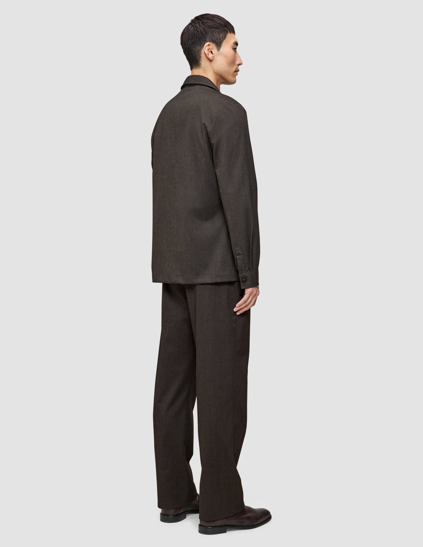 A man seen from the side wearing an Atelier Overshirt Dark Brown in a heavyweight textured fabric with matching trousers and brown leather shoes.