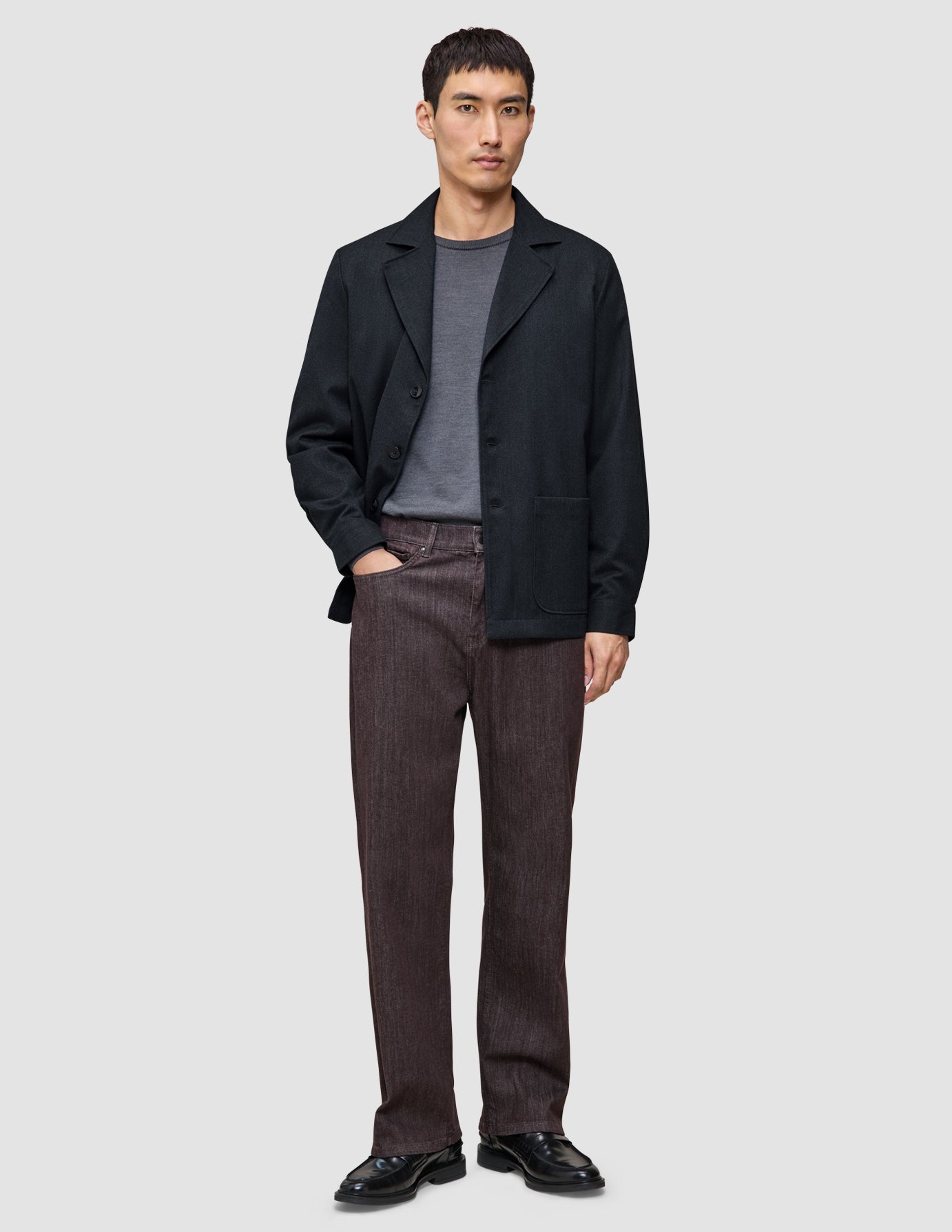 A man wearing a dark navy Atelier Overshirt over a grey t-shirt, dark trousers, and black dress shoes.