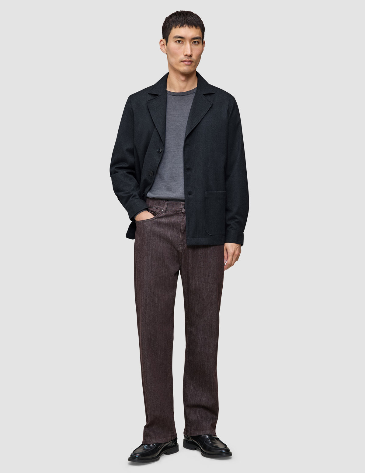 A man wearing a dark navy Atelier Overshirt over a grey t-shirt, dark trousers, and black dress shoes.