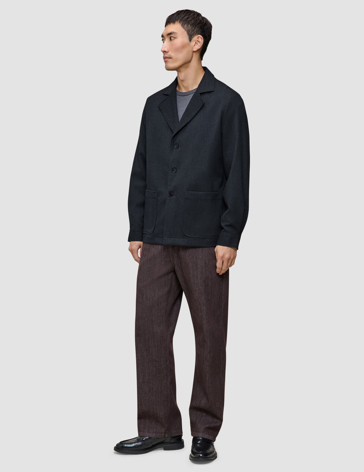 A person wearing a heavyweight, textured Atelier Overshirt Dark Navy over a grey t-shirt, paired with brown trousers and black loafers.
