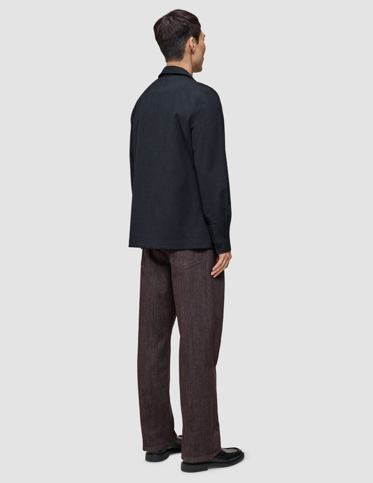 A person seen from behind, wearing an Atelier Overshirt Dark Navy in a heavyweight texture, paired with dark brown trousers and black dress shoes.