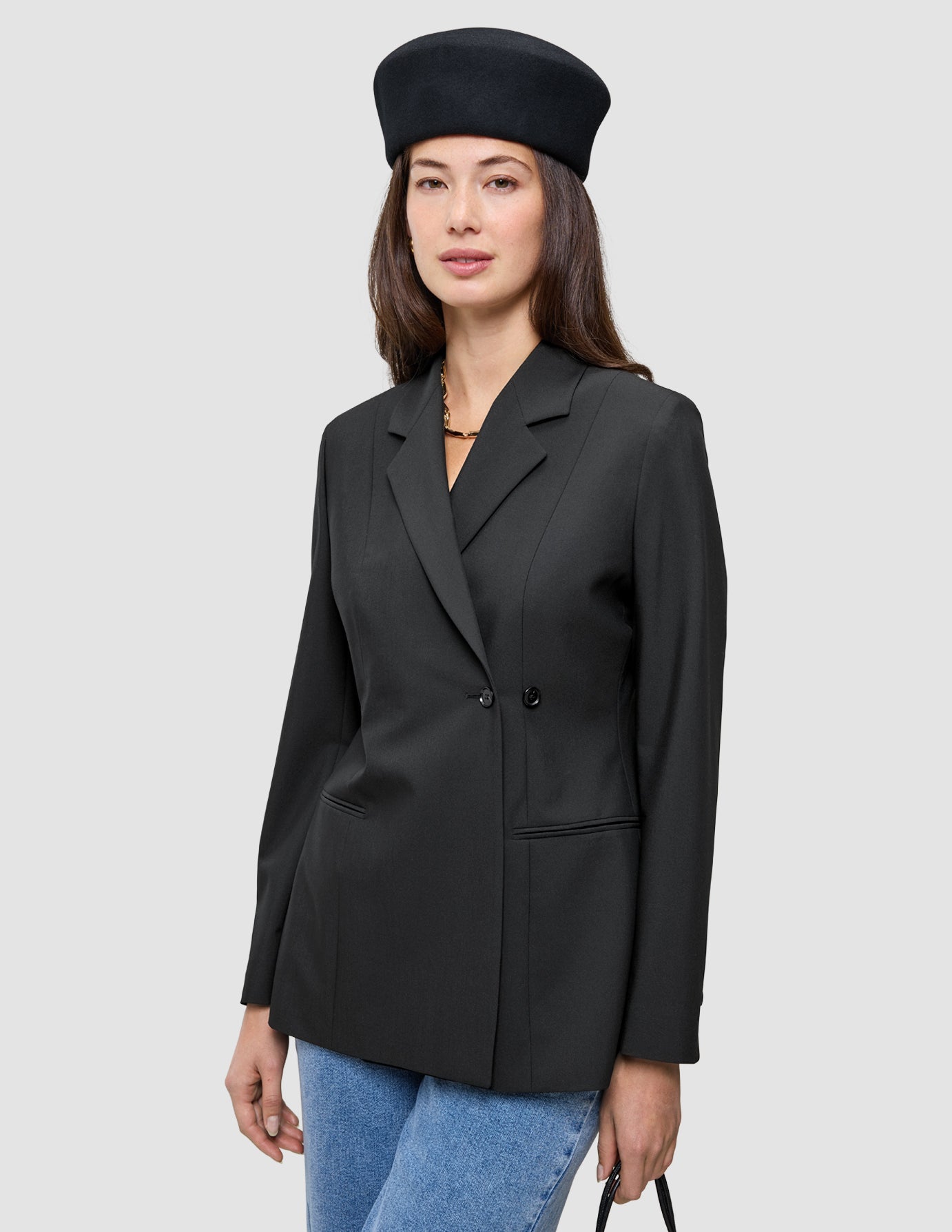 A person wearing a black Women’s Avira Blazer double-breasted blazer, blue jeans, and a black beret in the style of Scandinavian design.
