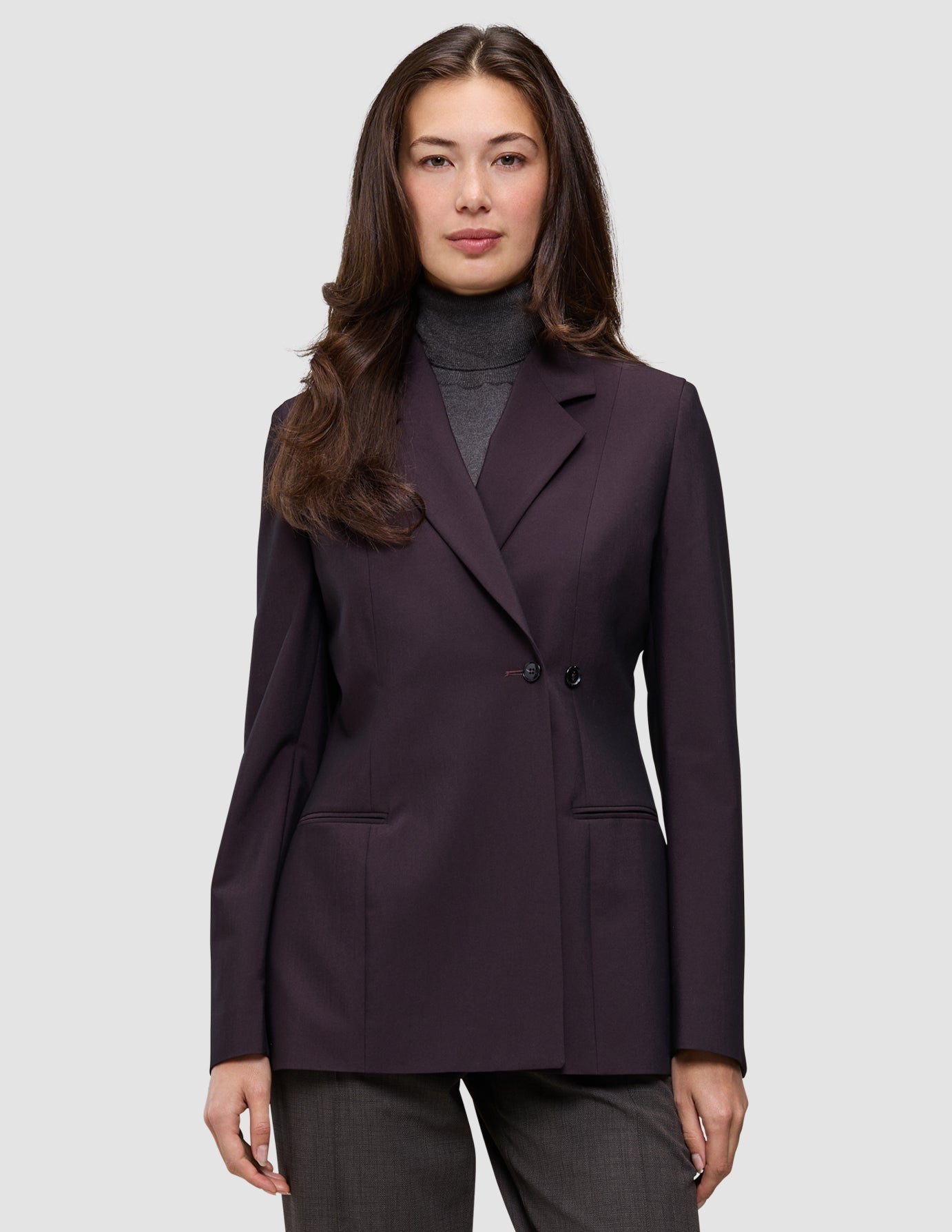 A person wearing a dark burgundy Women’s Avira Blazer Burgundy Berry double-breasted blazer over a grey turtleneck, embodying Scandinavian design.